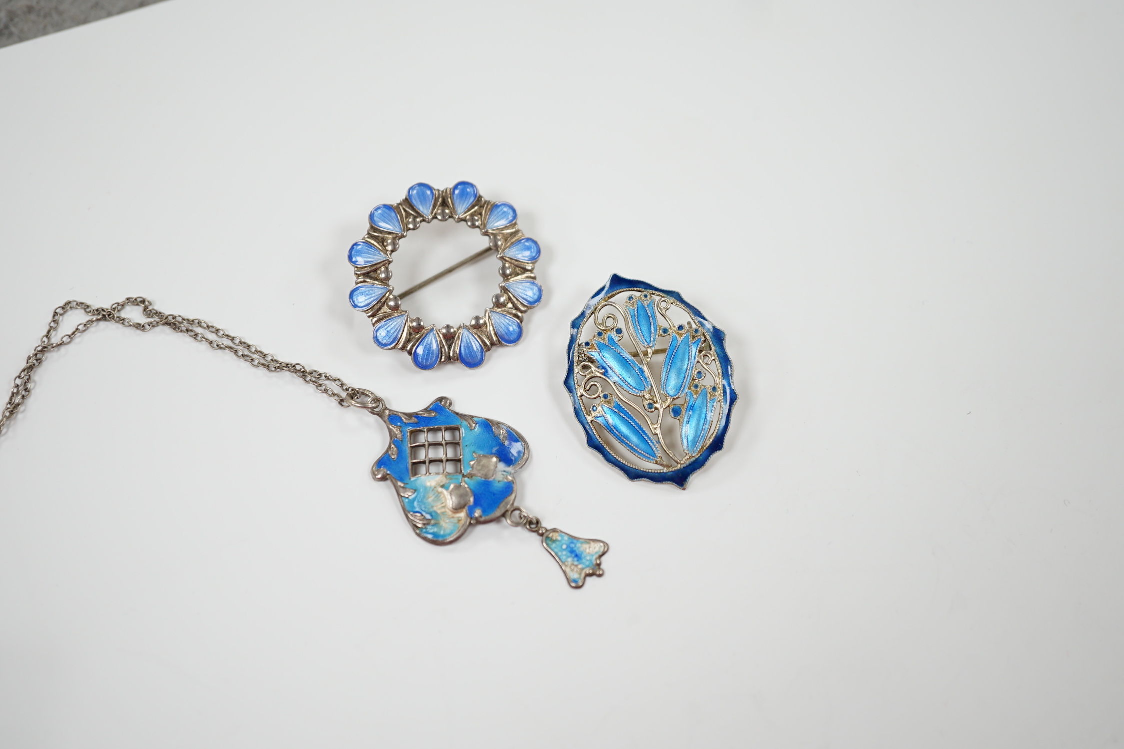 A George V silver and enamel set drop pendant (a.f.), 40mm on a white metal chain and two white metal and enamel brooches, one stamped sterling.